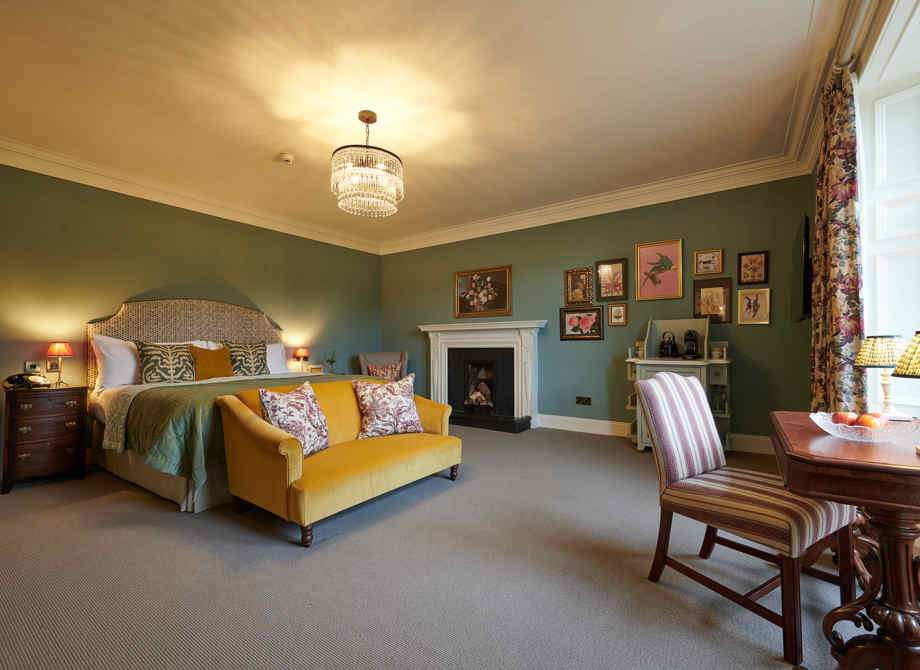 Inviting Junior Suite bedroom at the Cromlix Hotel in Dunblane, with a comfortable bed, a yellow sofa, a fireplace, and elegant furnishings.