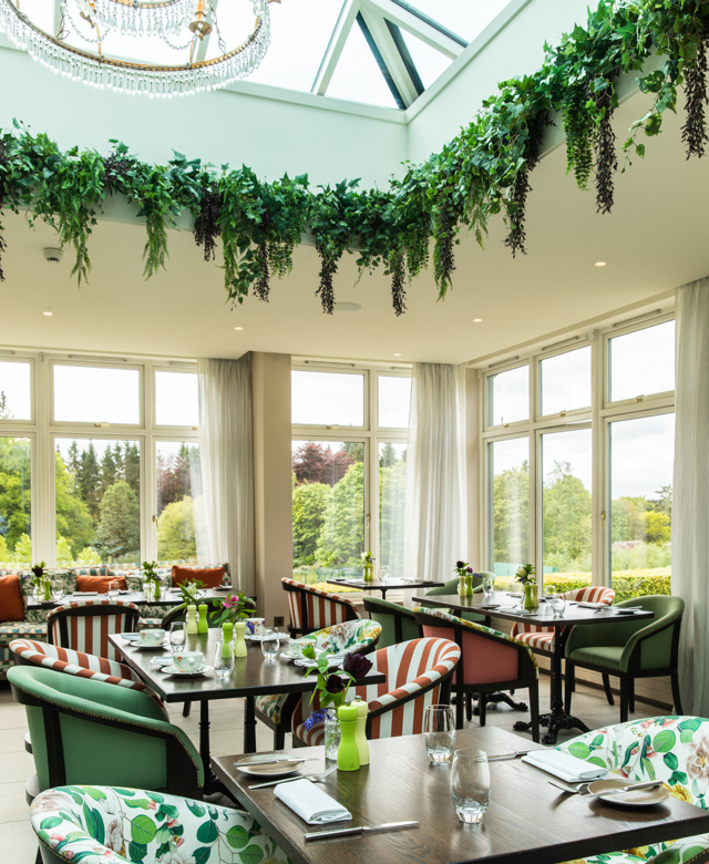 Interior of the Glasshouse restaurant at Cromlix Hotel, showcasing bright decor and garden scenery.