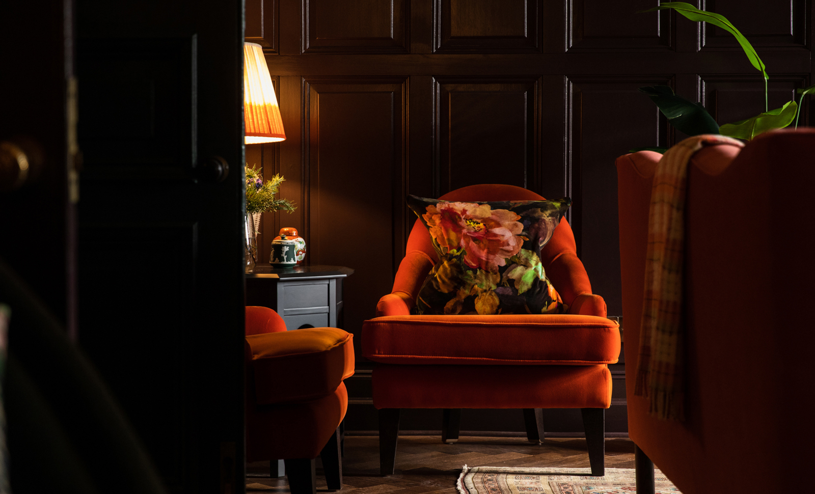 Cozy seating area at Cromlix Hotel, featuring a vibrant orange armchair with a bold floral cushion, warm lighting from a table lamp, and dark wooden panelling creating a luxurious, inviting ambiance.